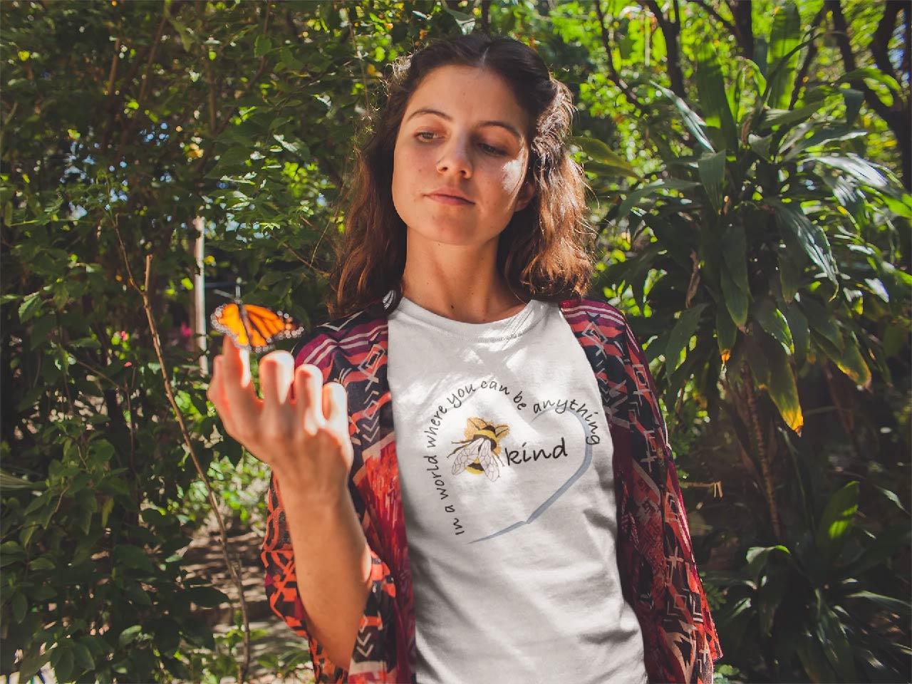 Girl wearing 'In a world wear you can be anything, be kind' T-shirt and watching a butterfly sit on her hand